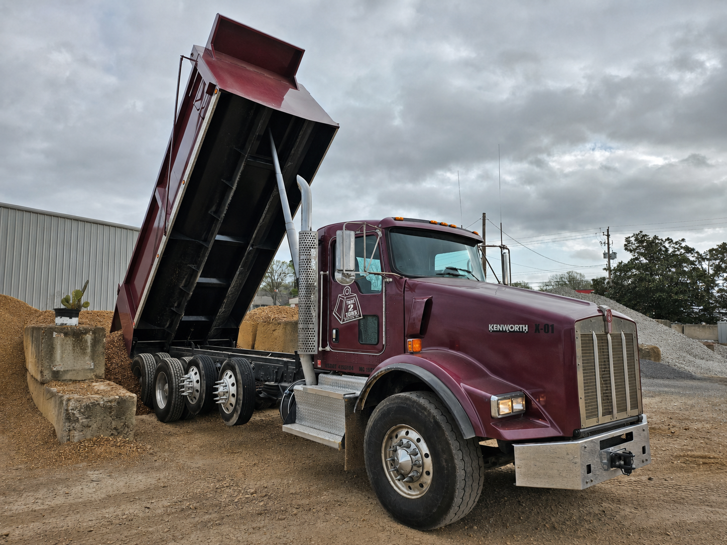 Maroon Tare 2 Tons Xpress dump truck with its bed raised at a material yard